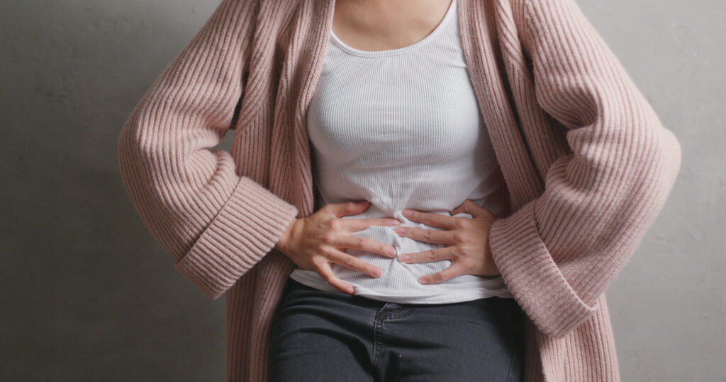 Femme en pull rose appuyant sur son abdomen avec les deux mains en raison d'un inconfort digestif