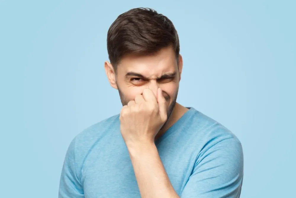 Un homme en t-shirt bleu se couvre le nez avec un geste de mécontentement dû à une mauvaise odeur