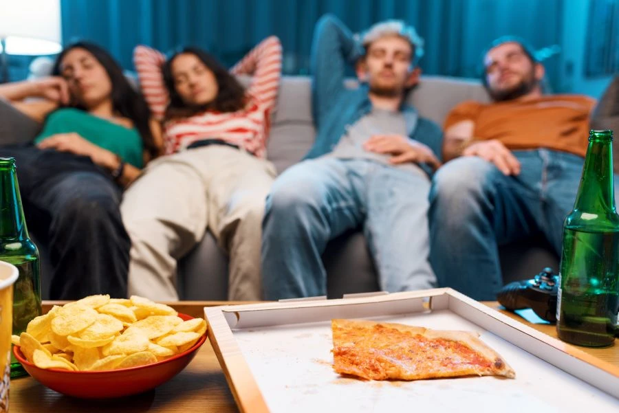 quatre personnes allongées sur le canapé après avoir mangé une pizza et des frites