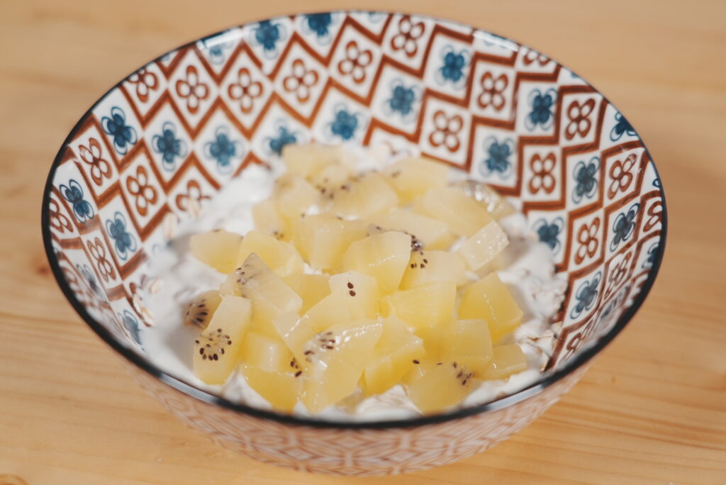 Bol de kéfir avec flocons d’avoine, garni de morceaux d’ananas et de kiwi.