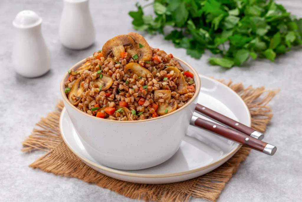 Bol de sarrasin cuisiné avec des légumes et des champignons, servi chaud dans un plat blanc.