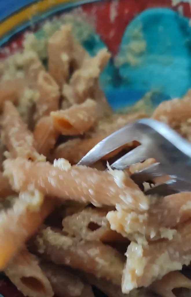 Pâtes servies dans une assiette, accompagnées d’une sauce crémeuse, avec une fourchette en train de les saisir.