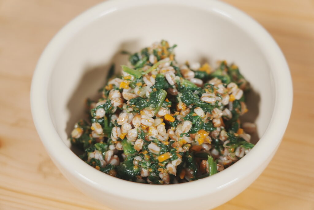 Bol d’épeautre mélangé avec des épinards, des carottes et des légumes, servi dans un petit récipient blanc.