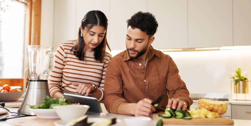 Couple en cuisine consultant une recette sur tablette avec légumes frais